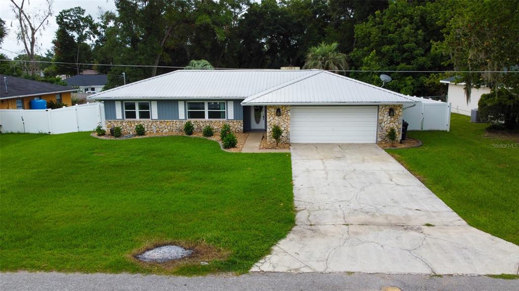 A single-story house with a metal roof, stone facade, and a concrete driveway — 5072 SE 27TH STREET, OCALA, FL