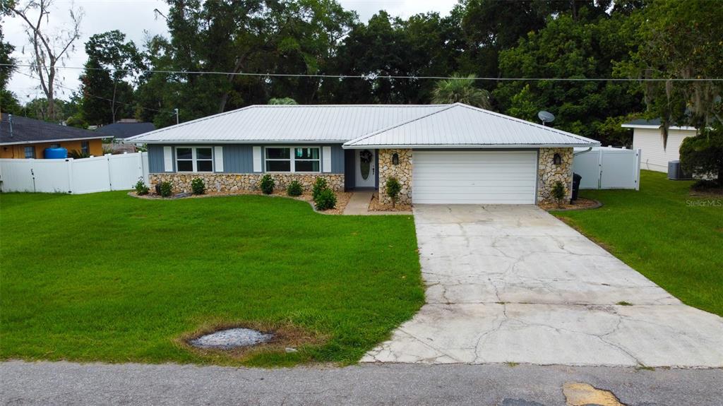 A single-story house with a white metal roof, stone accents, and a concrete driveway — 5072 SE 27TH STREET, OCALA, FL