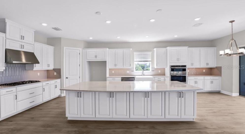 A modern kitchen features white cabinetry, a large central island, stainless steel appliances, and wood flooring — 26909 VICTORIA PLACE, PUNTA GORDA, FL