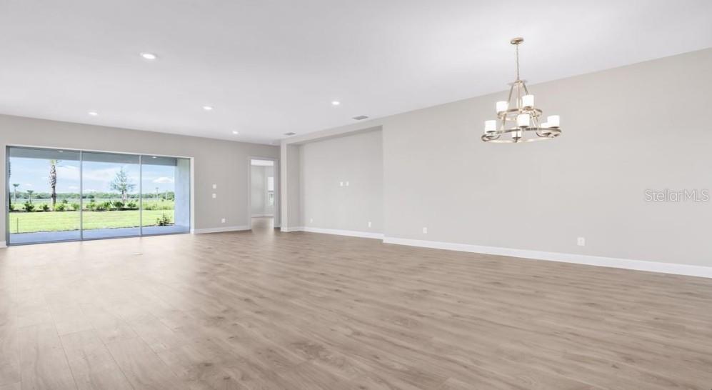 A spacious living room features light wood-look flooring, a chandelier, and large sliding glass doors — 26909 VICTORIA PLACE, PUNTA GORDA, FL