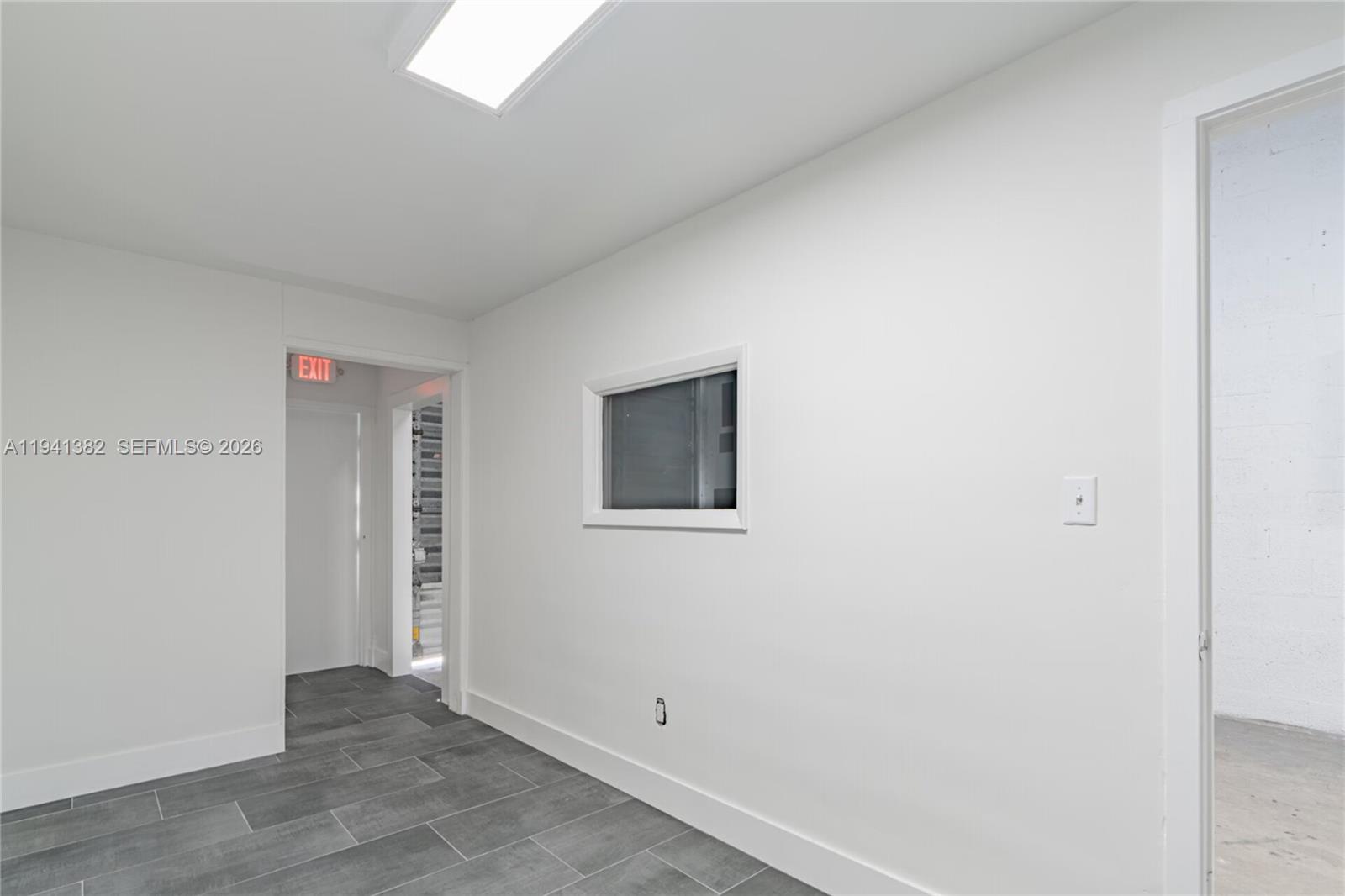A white-walled room features gray tile flooring, a small interior window, and two doorways — 569 W 28th St, Hialeah FL 33010, HIALEAH, FL