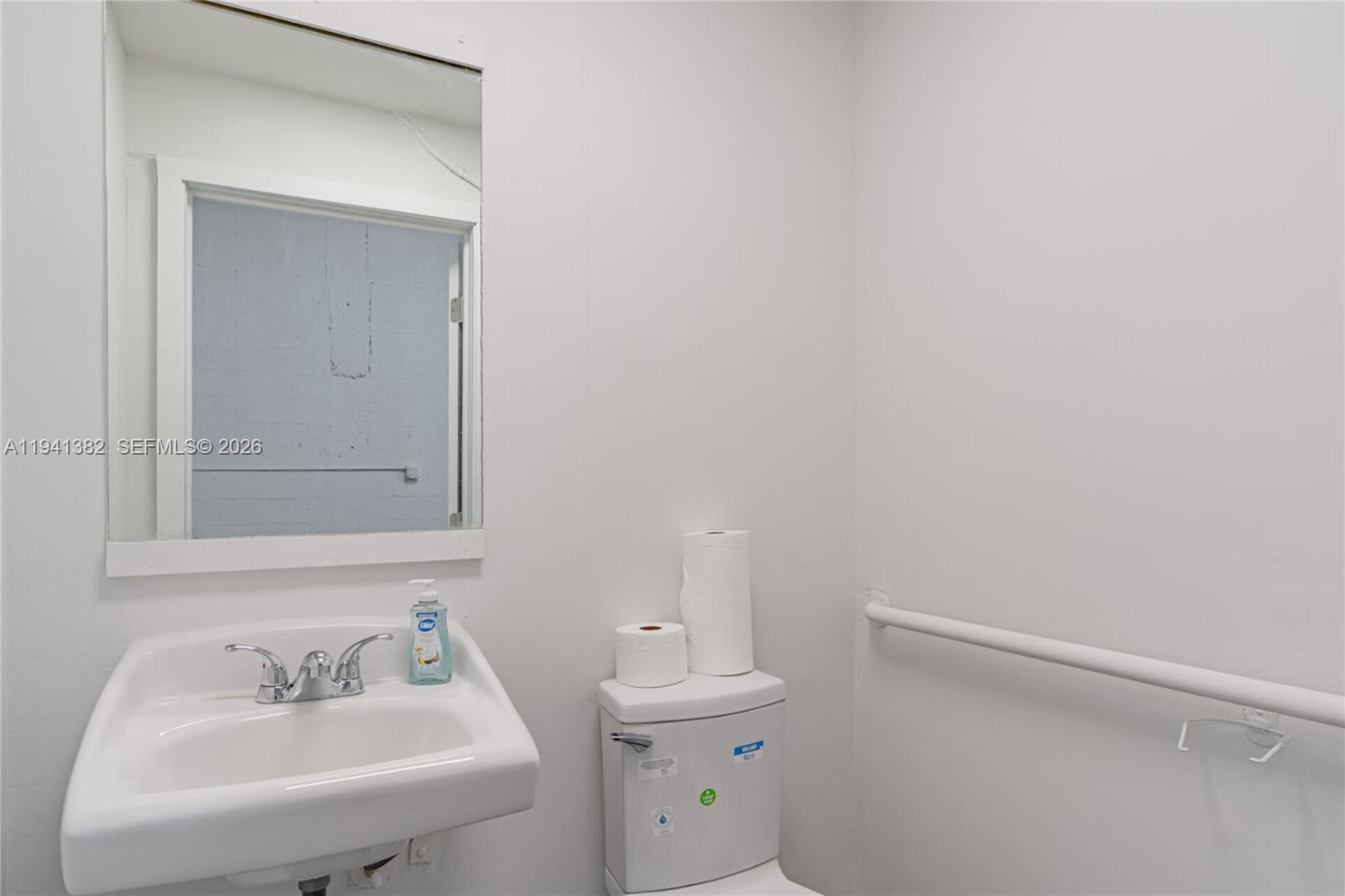 A small bathroom features a white wall-mounted sink, a toilet, and a grab bar — 569 W 28th St, Hialeah FL 33010, HIALEAH, FL