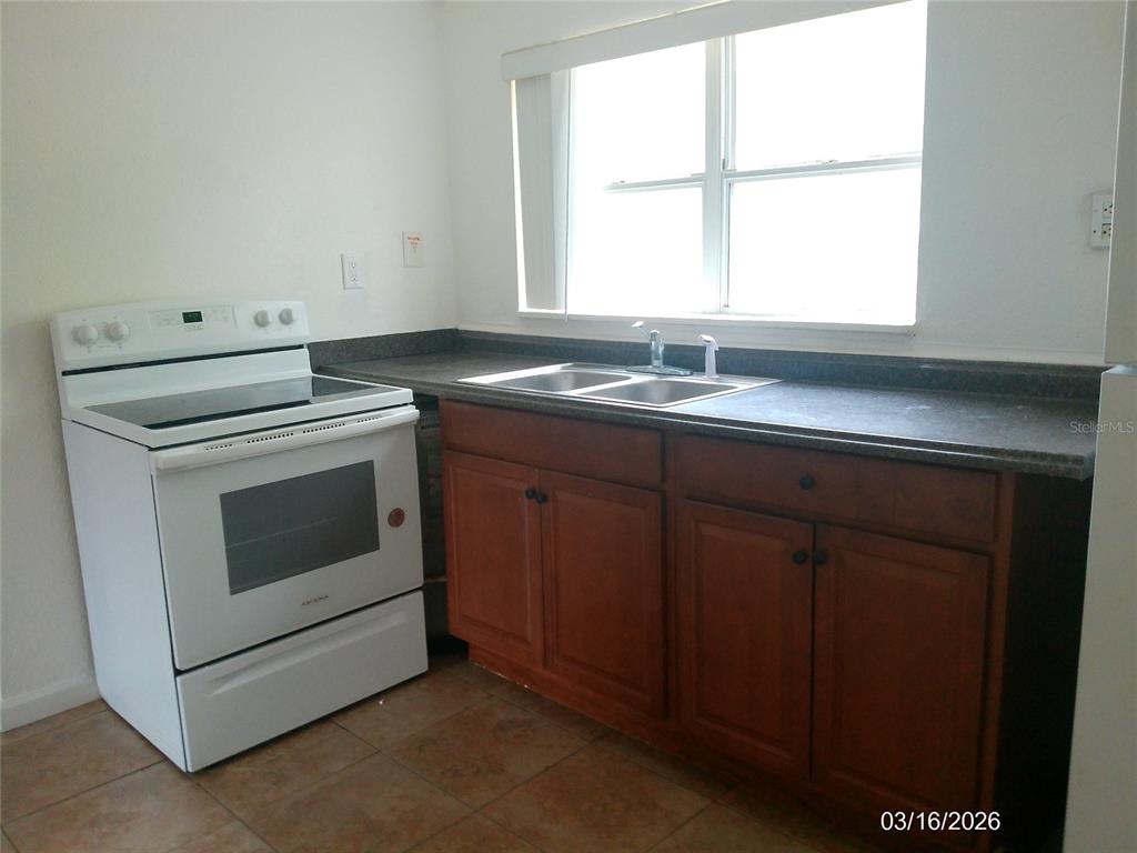 A kitchen features a white electric stove, wooden cabinets, a double sink, and tiled floors — 808 S CENTRAL AVENUE S, LAKELAND, FL
