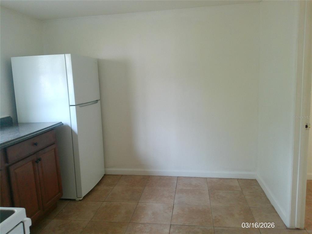 A white refrigerator stands next to wooden cabinets in a kitchen with tiled flooring — 808 S CENTRAL AVENUE S, LAKELAND, FL