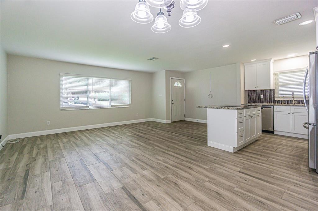 An open-concept living area features light wood-look flooring, a kitchen island, and a chandelier — 925 CEDARWOOD AVENUE, DUNEDIN, FL