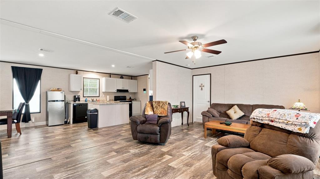 An open-concept living room and kitchen feature wood-look flooring, a ceiling fan, and brown furniture — 6988 N PALMER WAY, HERNANDO, FL