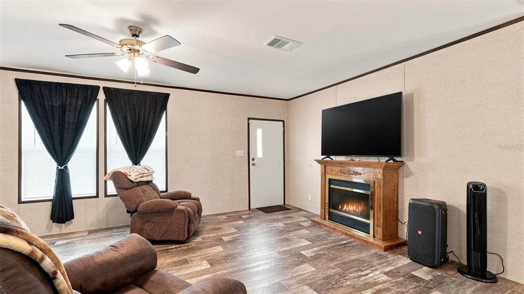 A living room features wood-look flooring, a fireplace with a television above, and a ceiling fan — 6988 N PALMER WAY, HERNANDO, FL