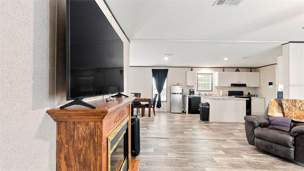 A living room with a fireplace and television opens into a kitchen with white cabinetry — 6988 N PALMER WAY, HERNANDO, FL