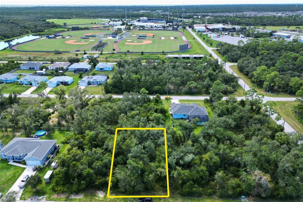 An aerial view shows a rectangular, wooded vacant lot outlined in yellow near residential homes — 2157 TEA STREET, PORT CHARLOTTE, FL