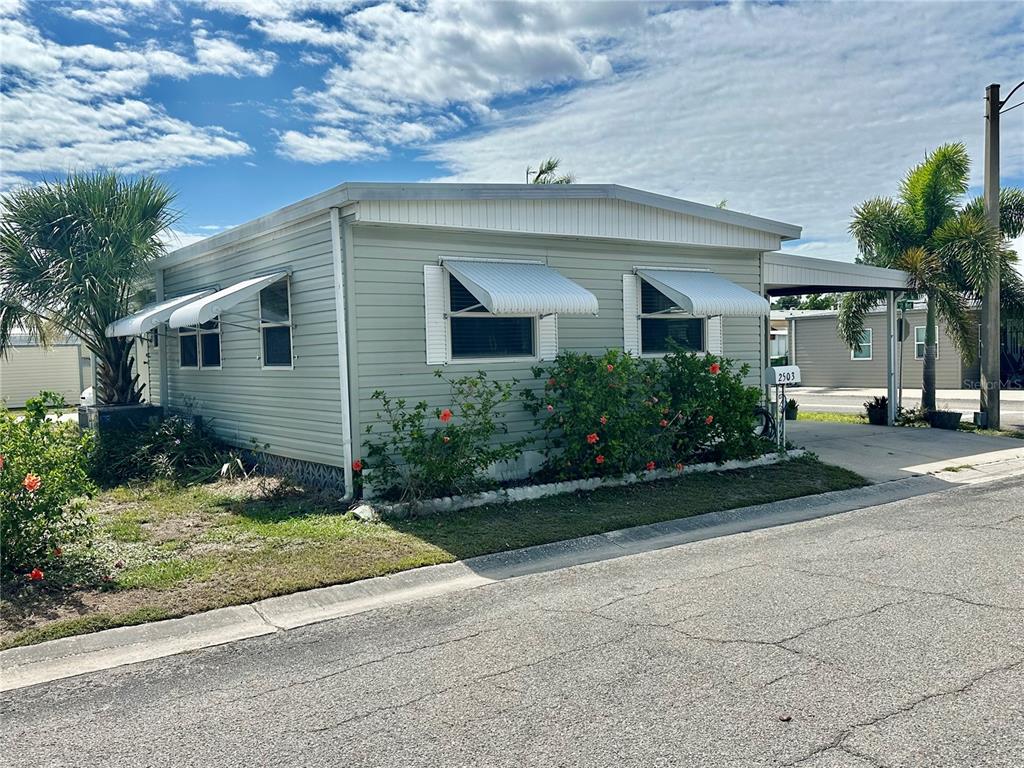 A light green mobile home with white window awnings and a carport sits on a street — 2503 16TH STREET W, BRADENTON, FL