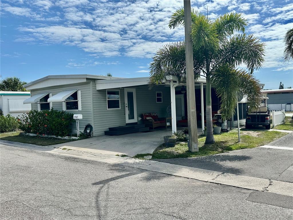 A light green manufactured home features a covered carport, a palm tree, and a golf cart — 2503 16TH STREET W, BRADENTON, FL