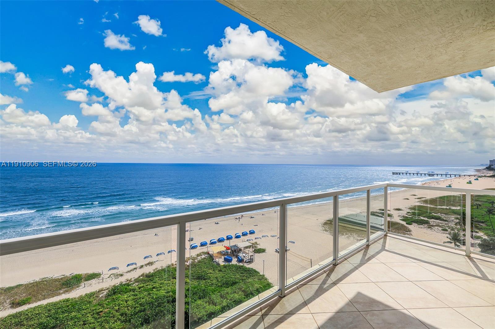 A balcony with a glass railing overlooks a sandy beach and the ocean — 704 N Ocean Blvd # 1001, Pompano Beach FL 33062, POMPANO BEACH, FL