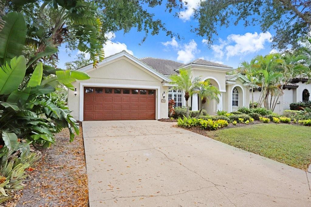 A single-story house with a brown garage door, beige stucco exterior, and lush landscaping — 1161 MARINA DRIVE, TARPON SPRINGS, FL