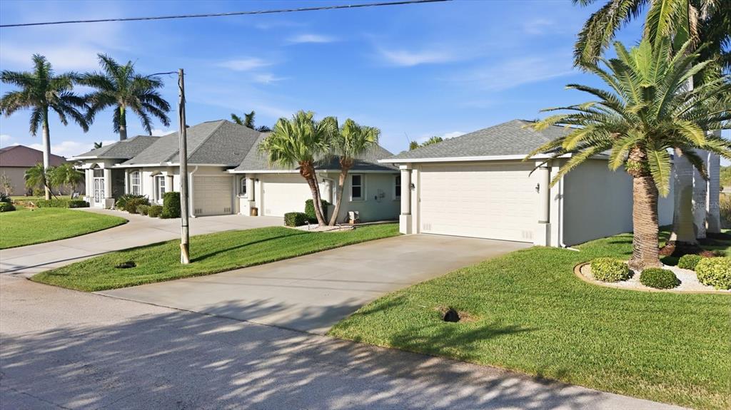 A view of a house exterior featuring a driveway, a garage, and several palm trees — 8050 TRACY CIRCLE, PORT CHARLOTTE, FL