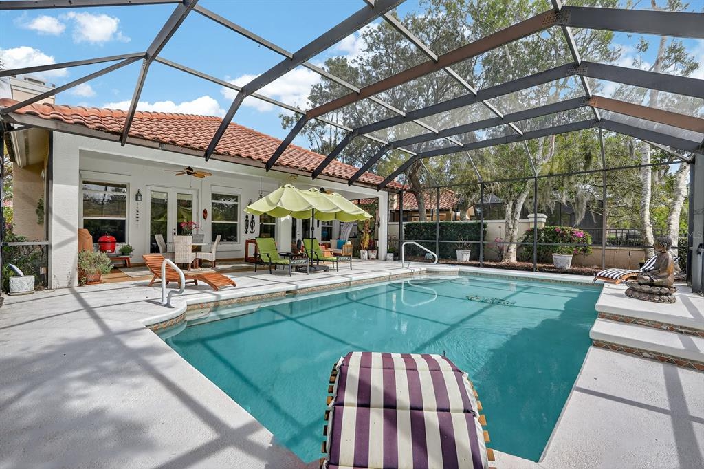A screened-in swimming pool patio features lounge chairs, a yellow umbrella, and a lake view — 11 LAGUNA COURT, PALM COAST, FL