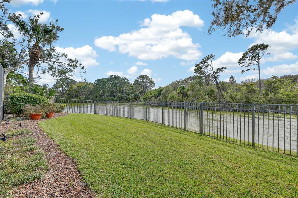 A screened-in swimming pool patio features lounge chairs, a yellow umbrella, and a wooded view — 11 LAGUNA COURT, PALM COAST, FL