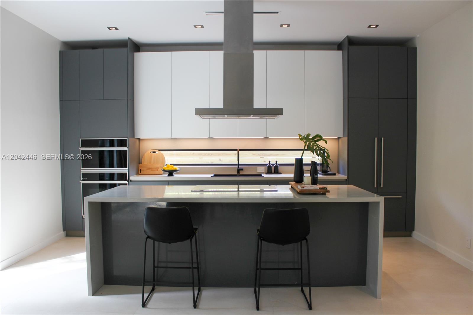 A modern kitchen features dark grey cabinetry, white upper cabinets, a central island, and stainless appliances — 3540 Oak Ave, Miami FL 33133, MIAMI, FL