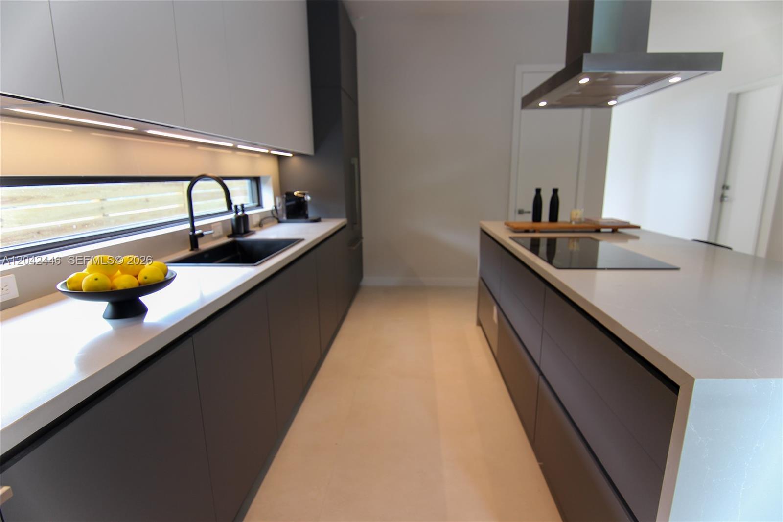 A modern galley kitchen features dark cabinetry, white countertops, a black sink, and a cooktop — 3540 Oak Ave, Miami FL 33133, MIAMI, FL