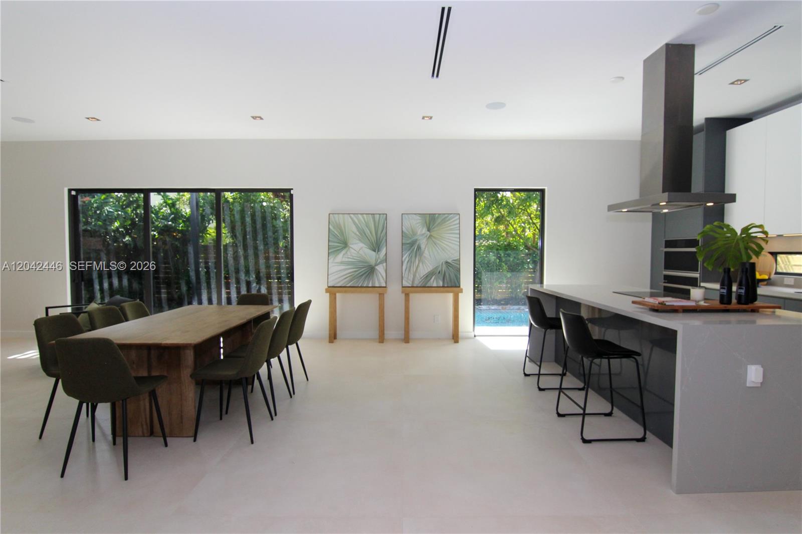 A modern open-concept kitchen and dining area features a large island, wooden table, and patio — 3540 Oak Ave, Miami FL 33133, MIAMI, FL