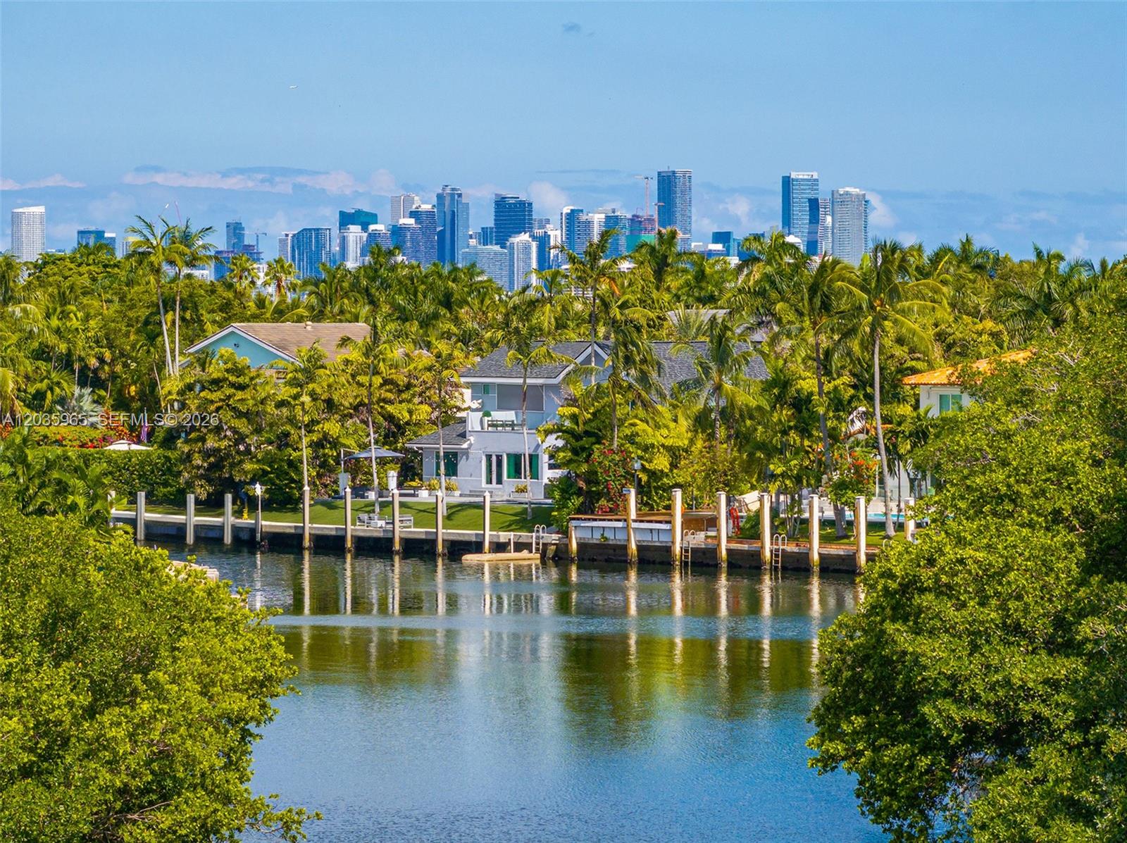 A waterfront house with a dock is surrounded by trees with a city skyline behind — 6944 Sunrise Ter, Coral Gables FL 33133, CORAL GABLES, FL