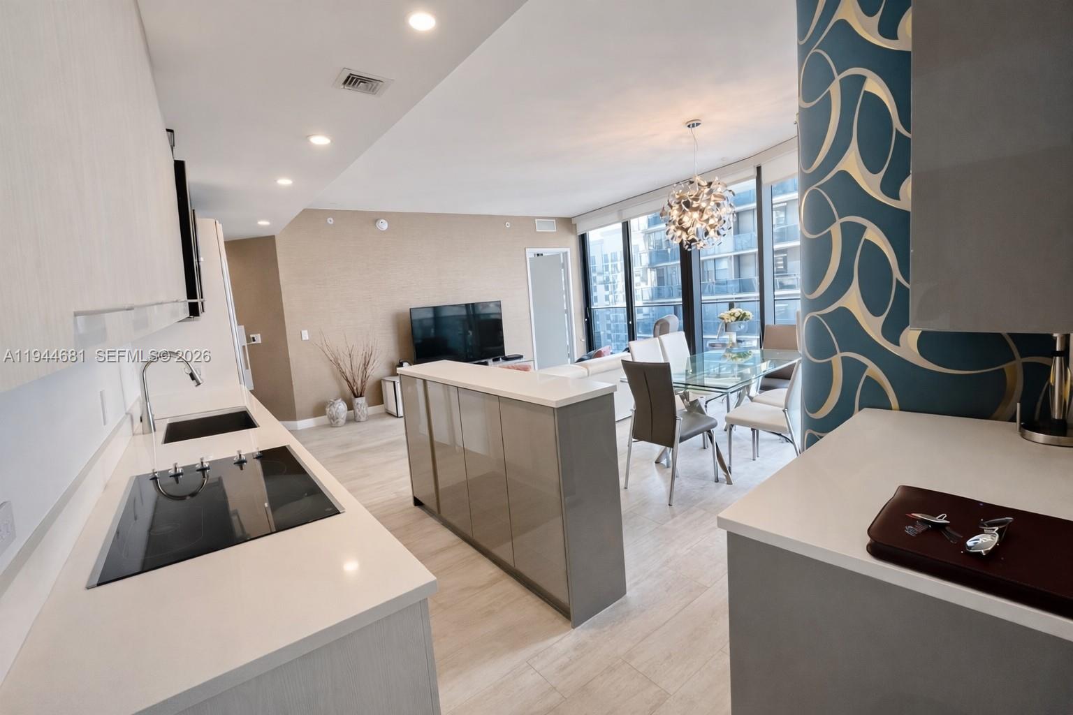 A modern kitchen with white countertops and gray cabinetry overlooks an open-concept dining and living area — 45 SW 9th St # 3008, Miami FL 33130, MIAMI, FL