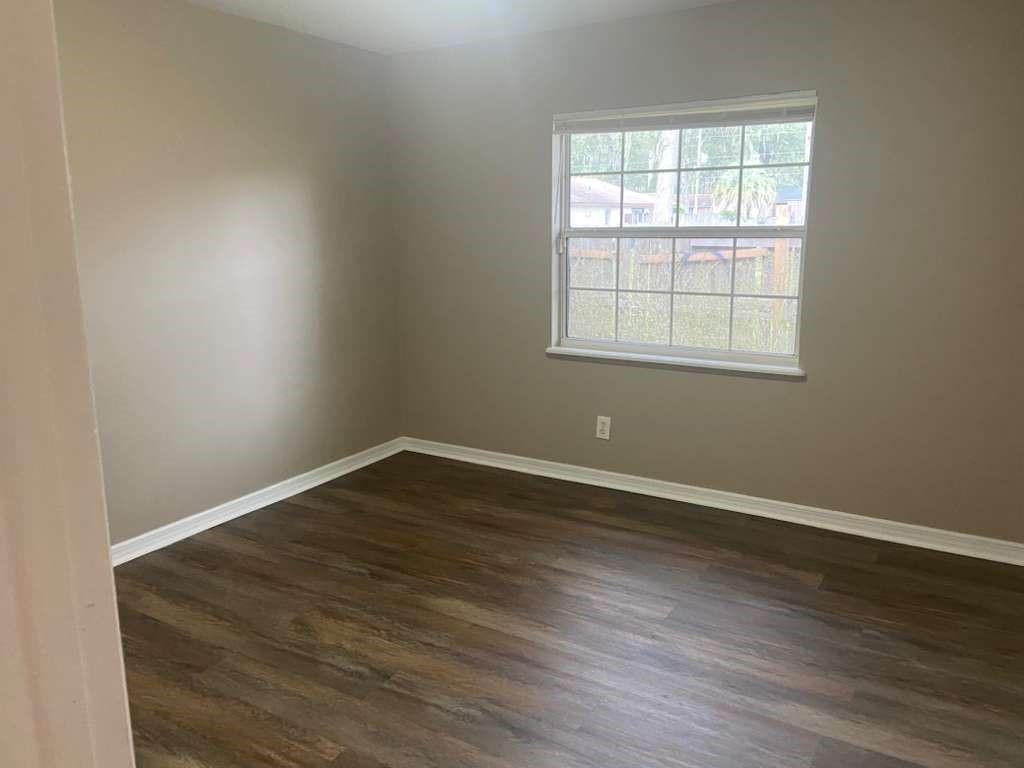 An empty bedroom with beige walls, white trim, and dark wood-look flooring — 1801 SE 40th Street Road, Ocala FL 34480, OCALA, FL