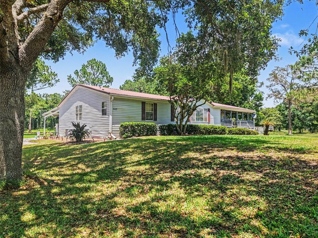 A single-story house with light-colored siding sits on a grassy lot under large trees — 5105 STAR LINE DRIVE, ST CLOUD, FL