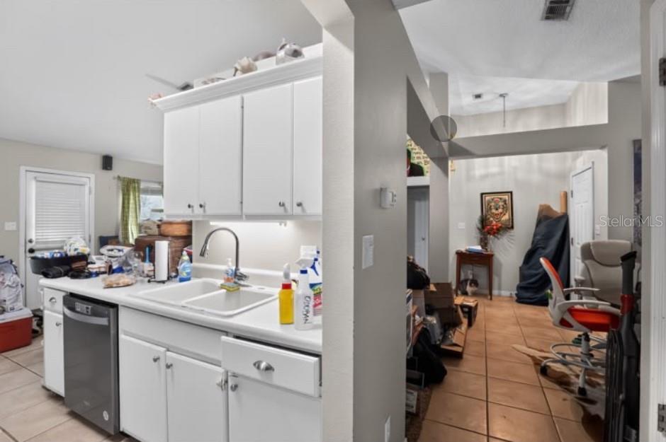 A kitchen with white cabinets and a stainless steel dishwasher overlooks a tiled living area — 4374 MARILYN COURT, GULF BREEZE, FL