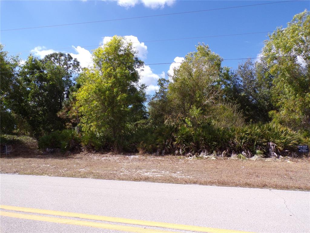 A vacant, wooded lot sits alongside a paved road under a blue sky — 12253 GREEN GULF BOULEVARD, PUNTA GORDA, FL
