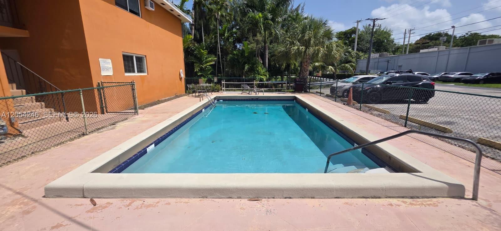 An outdoor rectangular swimming pool is situated next to an orange building and a parking lot — 7901 SW 64th Ave # 4, South Miami FL 33143, SOUTH MIAMI, FL