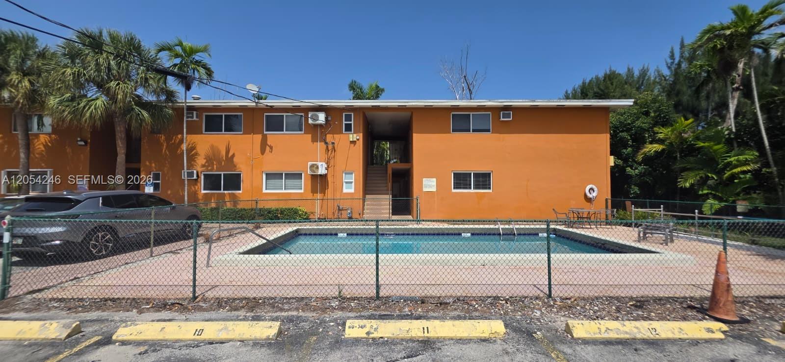 A two-story orange apartment building features a swimming pool enclosed by a chain-link fence — 7901 SW 64th Ave # 4, South Miami FL 33143, SOUTH MIAMI, FL