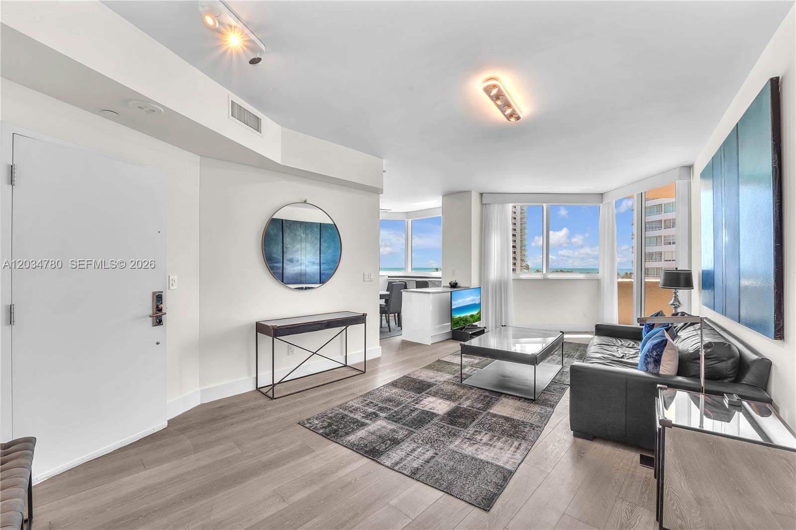 A modern living room features a black leather sofa, a glass coffee table, and ocean views — 300 S POINTE DR # 809, Miami Beach FL 33139, MIAMI BEACH, FL