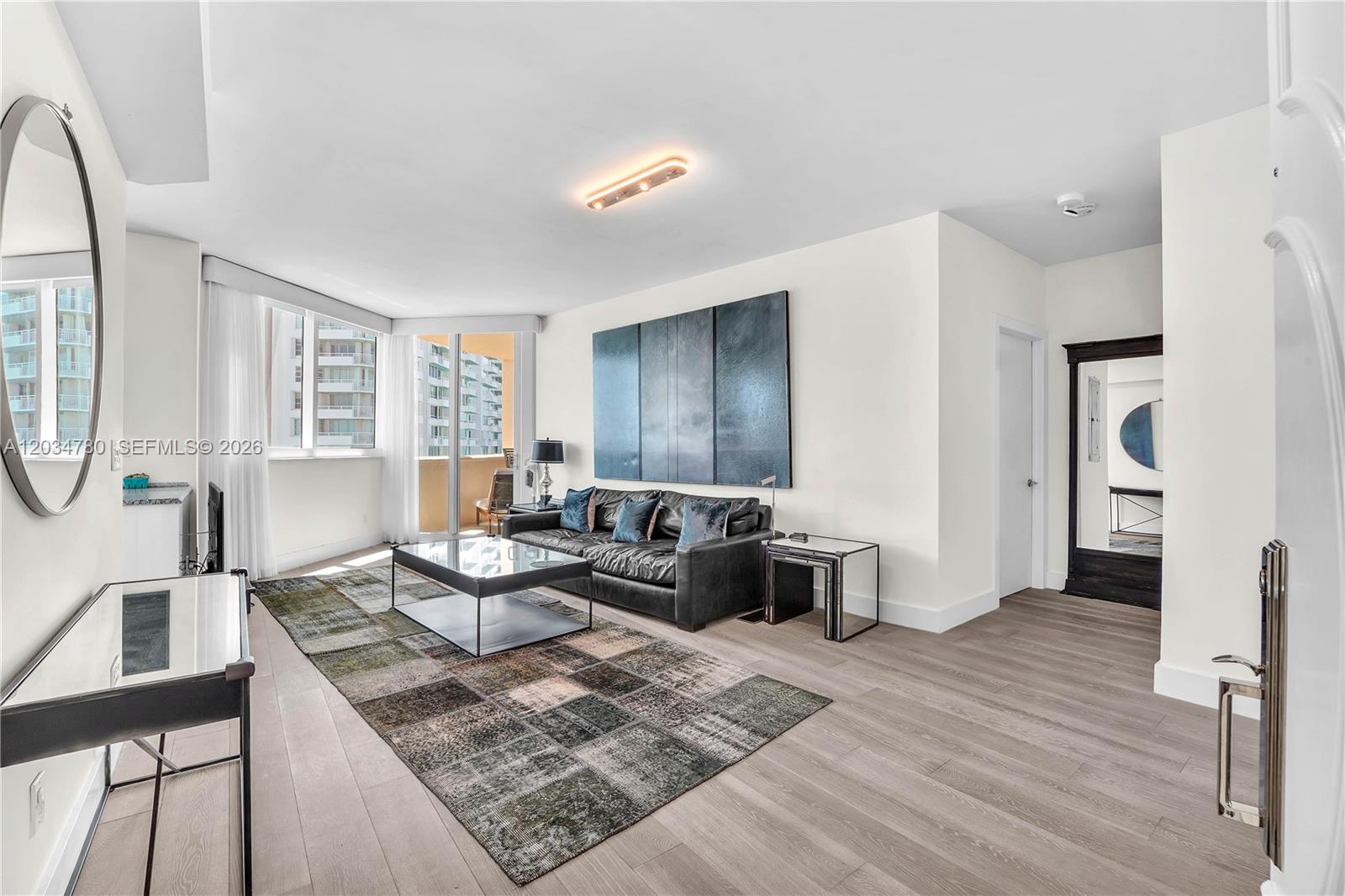 A modern living room features a dark leather sofa, a glass coffee table, and wood flooring — 300 S POINTE DR # 809, Miami Beach FL 33139, MIAMI BEACH, FL