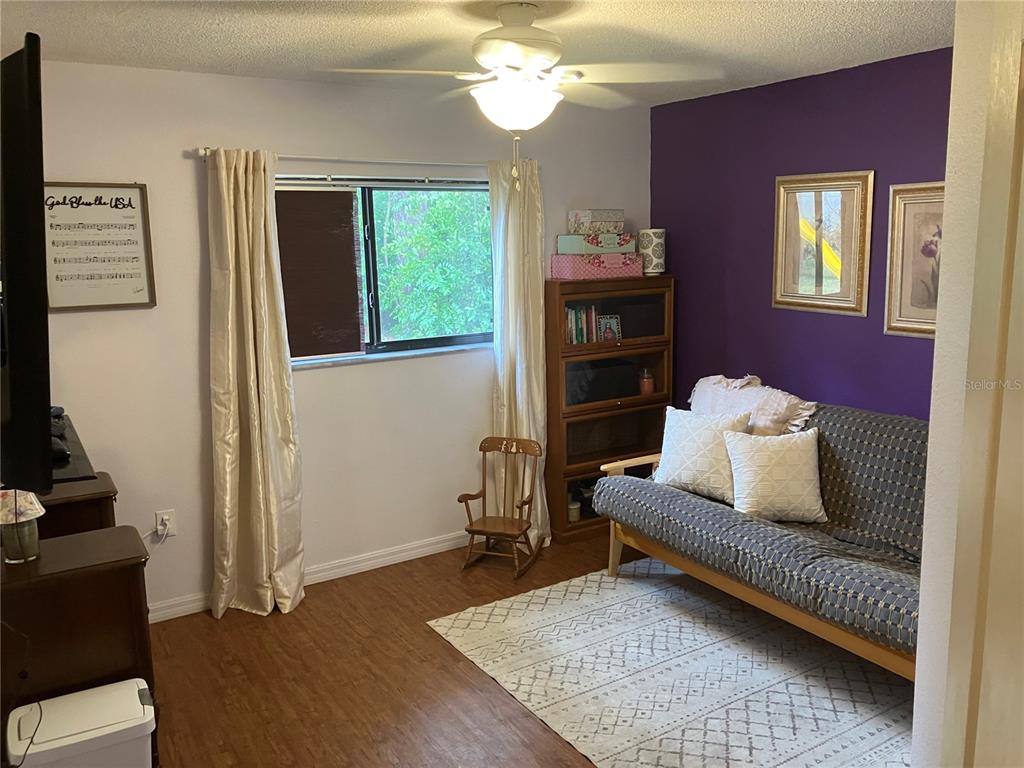 A room with wood-look flooring features a purple accent wall, a futon, and a bookcase — 14050 BRIGHTON STREET, SPRING HILL, FL
