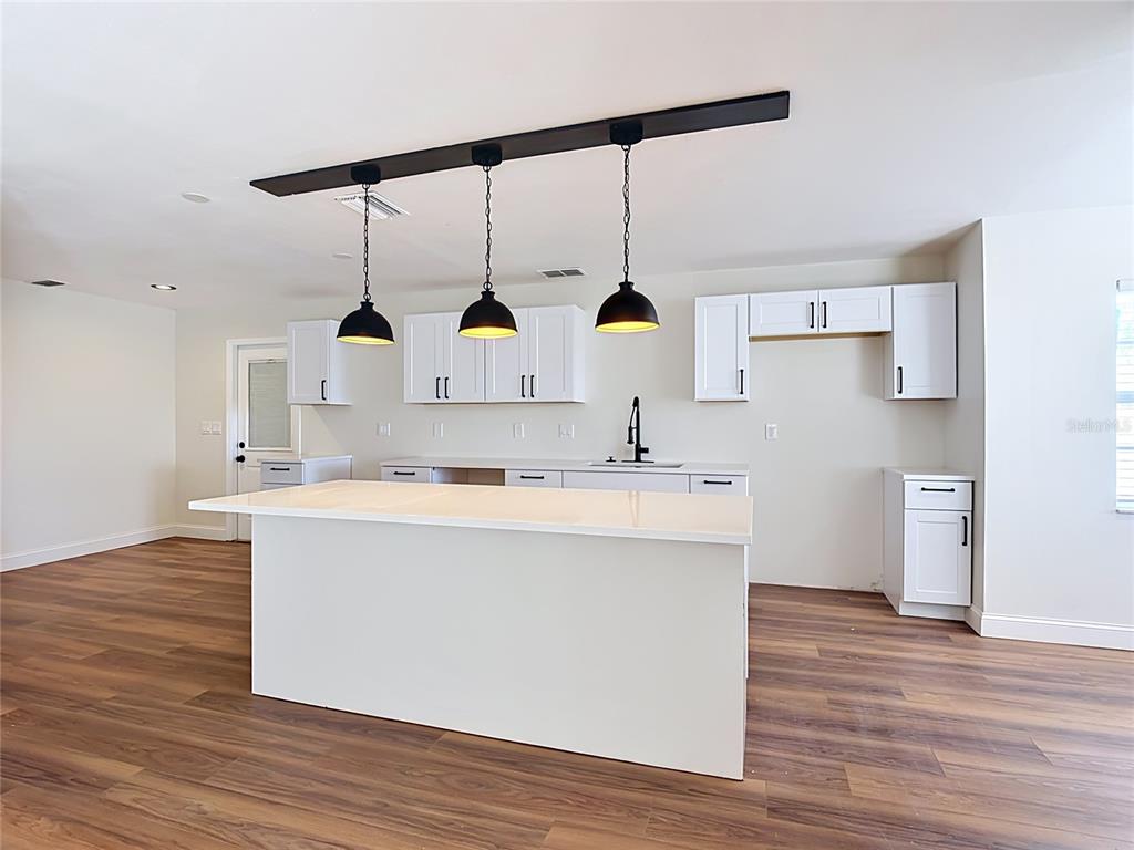 A kitchen features white cabinets, a large island, and three pendant lights over the counter — 7925 LAKE MABEL LOOP ROAD, DUNDEE, FL