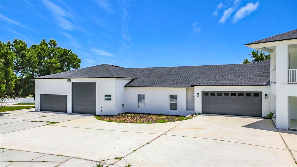 A white house exterior features three garage doors, a dark shingled roof, and concrete driveway — 7925 LAKE MABEL LOOP ROAD, DUNDEE, FL