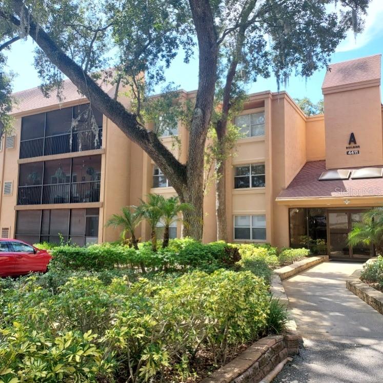A three-story tan apartment building with screened balconies and a paved walkway entrance — 4411 SHADY TERRACE LANE UNIT 209, TAMPA, FL