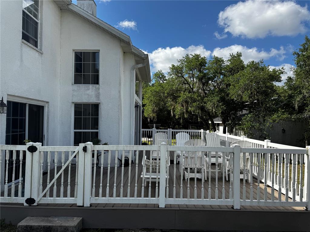 A white house with a wooden deck and white railing overlooks a backyard with trees — 1701 BERN CREEK LOOP, SARASOTA, FL