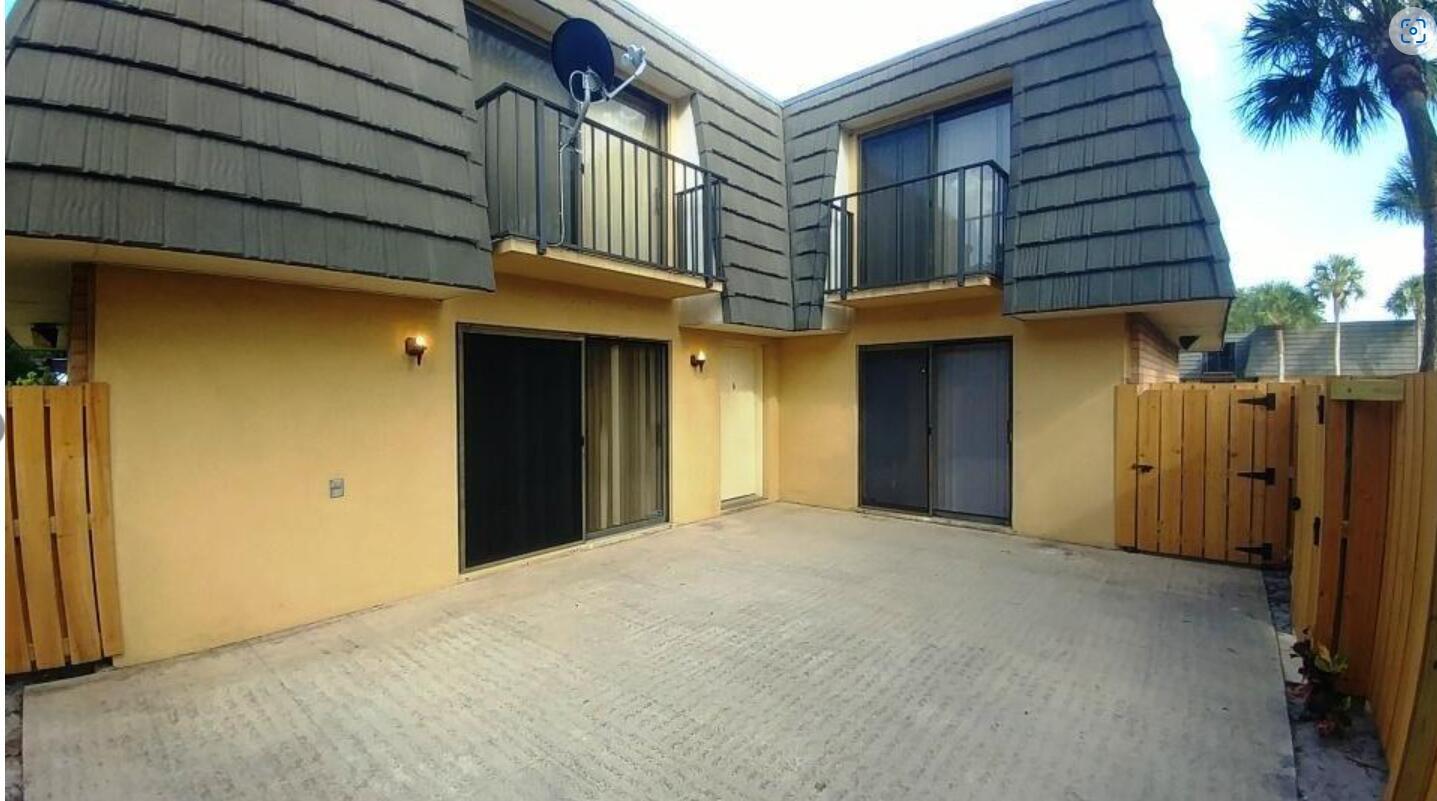 A two-story townhouse exterior features a concrete patio, sliding glass doors, and upper-level balconies — 221 2nd Way, West Palm Beach FL 33407, WEST PALM BEACH, FL