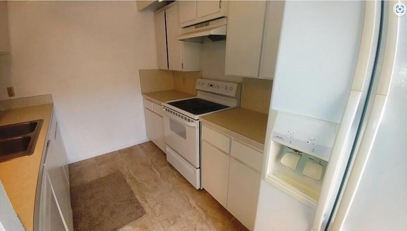 A galley-style kitchen features white cabinets, tan countertops, a white stove, and tile flooring — 221 2nd Way, West Palm Beach FL 33407, WEST PALM BEACH, FL