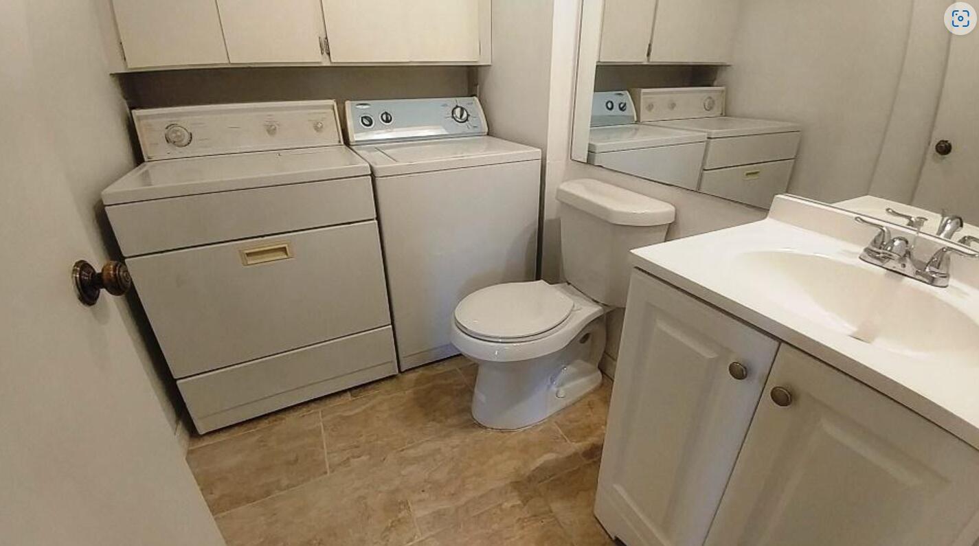 A bathroom features a white vanity, a toilet, and a side-by-side washer and dryer unit — 221 2nd Way, West Palm Beach FL 33407, WEST PALM BEACH, FL