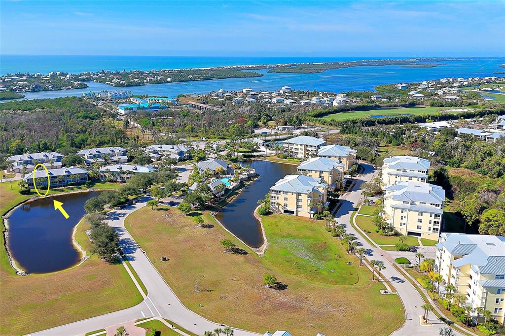 An aerial view shows a multi-story residential complex with a pond and coastal surroundings — 10700 LEMON CREEK LOOP UNIT 103, ENGLEWOOD, FL