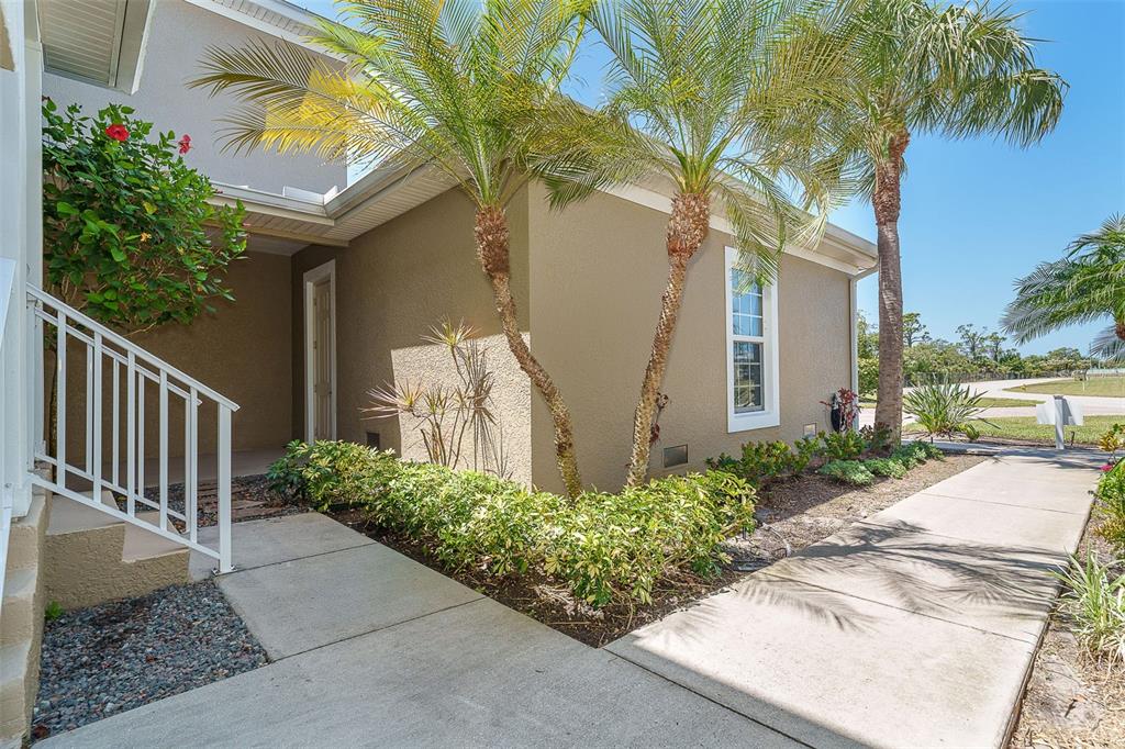 A concrete walkway leads to the entrance of a tan house with two palm trees — 10700 LEMON CREEK LOOP UNIT 103, ENGLEWOOD, FL