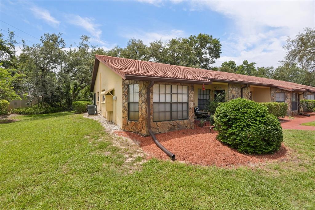 The exterior of a single-story house features a tiled roof, stone accents, and a lawn — 8626 SHADBLOW COURT UNIT 1, PORT RICHEY, FL