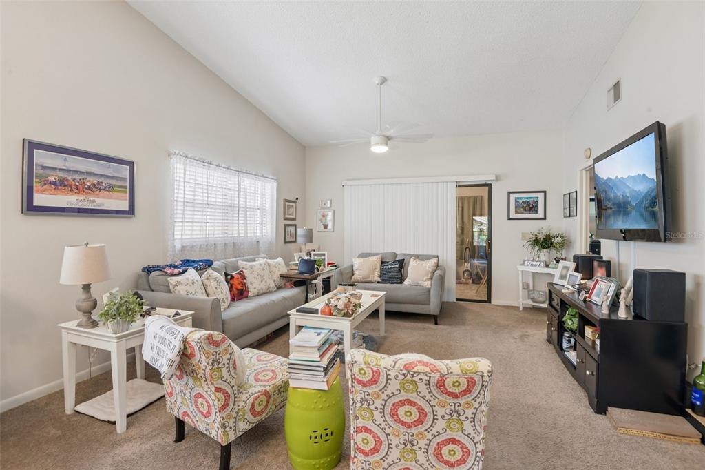 A living room features two gray sofas, patterned armchairs, a coffee table, and a television — 8626 SHADBLOW COURT UNIT 1, PORT RICHEY, FL
