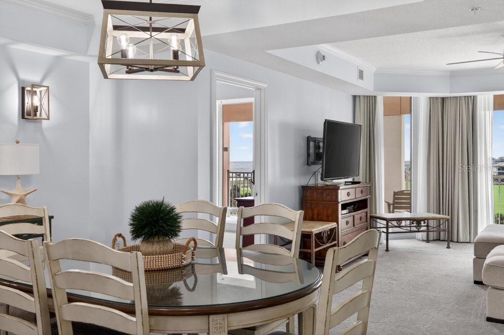 A dining area with a glass table and chandelier opens into a living room with balcony access — 200 OCEAN CREST DRIVE UNIT 517, PALM COAST, FL
