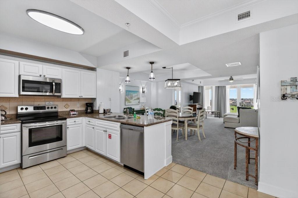 A kitchen with white cabinets and stainless steel appliances opens to a carpeted dining area — 200 OCEAN CREST DRIVE UNIT 517, PALM COAST, FL