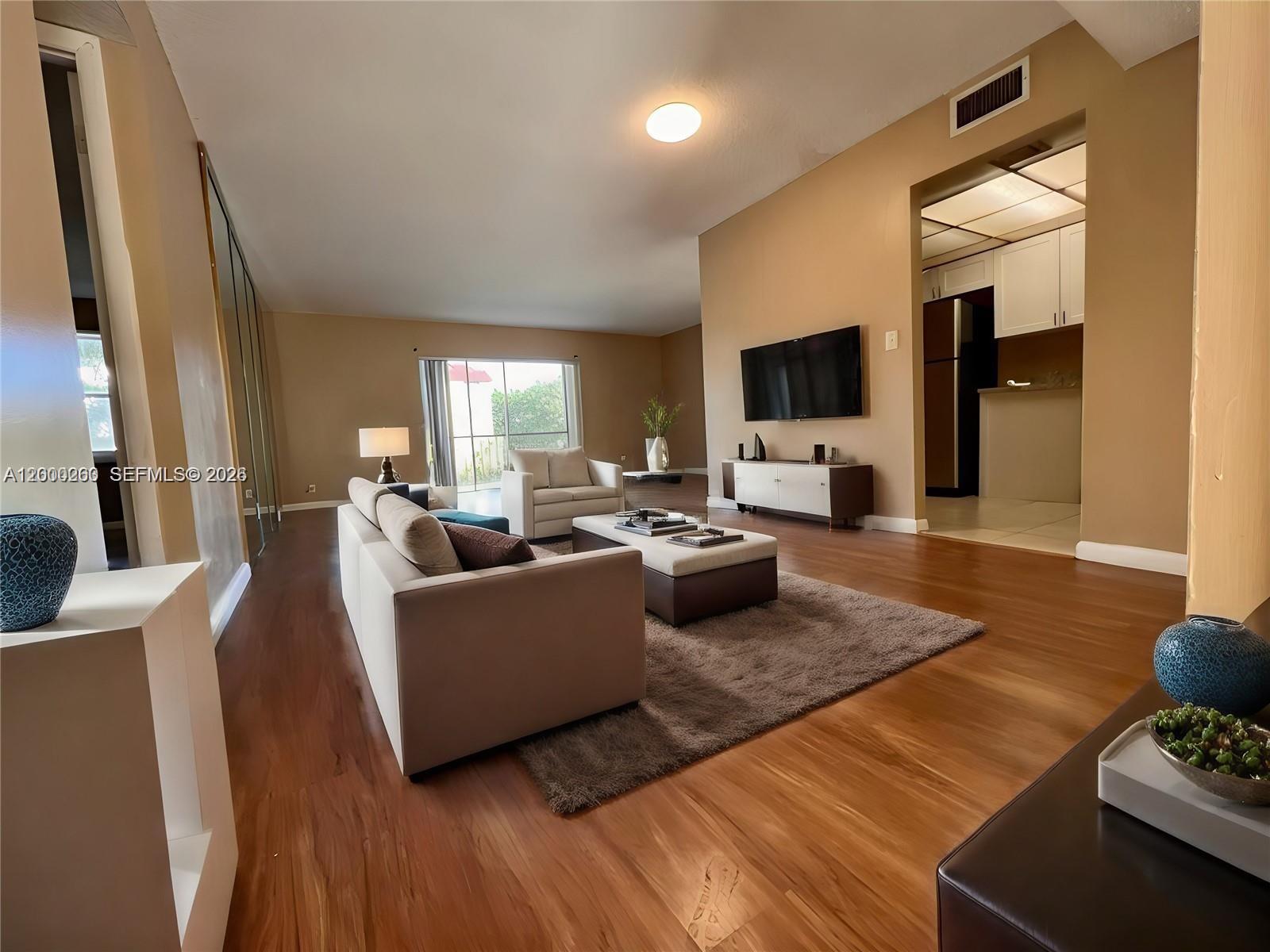 A living room features wood flooring, a beige sofa, a television, and an adjacent kitchen — 3300 Spanish Moss Ter # 206, Lauderhill FL 33319, LAUDERHILL, FL