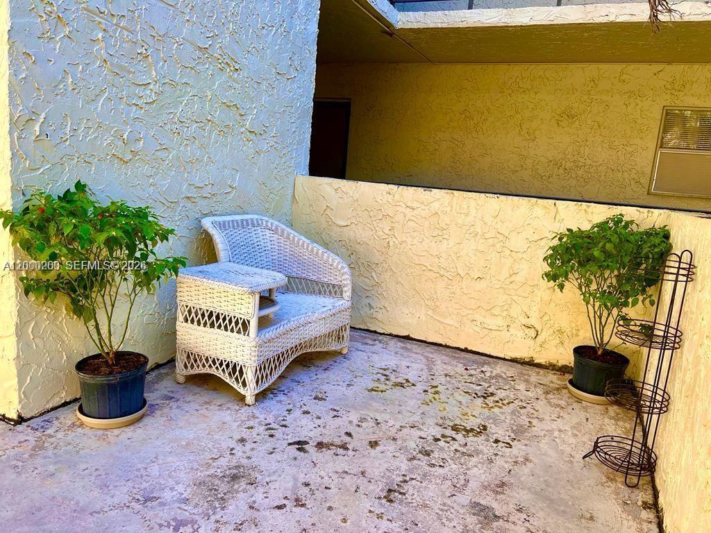 A white wicker chair sits on a concrete balcony with two potted plants — 3300 Spanish Moss Ter # 206, Lauderhill FL 33319, LAUDERHILL, FL