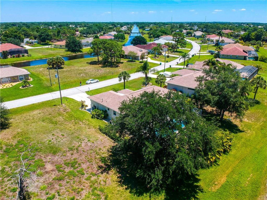 An aerial view shows a residential neighborhood with houses, a canal, and large trees — 155 LONG MEADOW LANE, ROTONDA WEST, FL